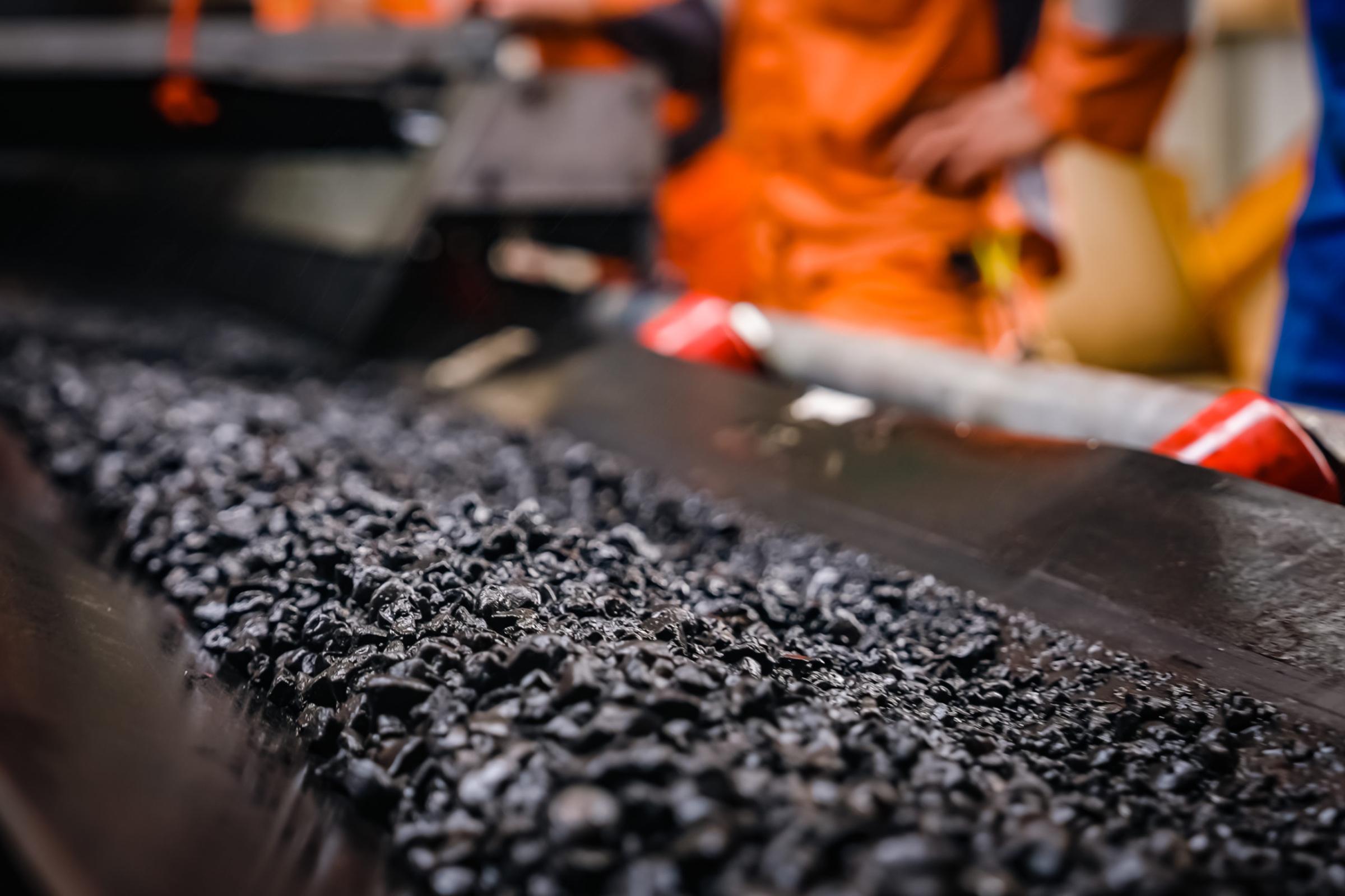 A worker stands beside a conveyor belt loaded with mineral-rich polymetallic nodules, overseeing the material flow in an industrial setting.