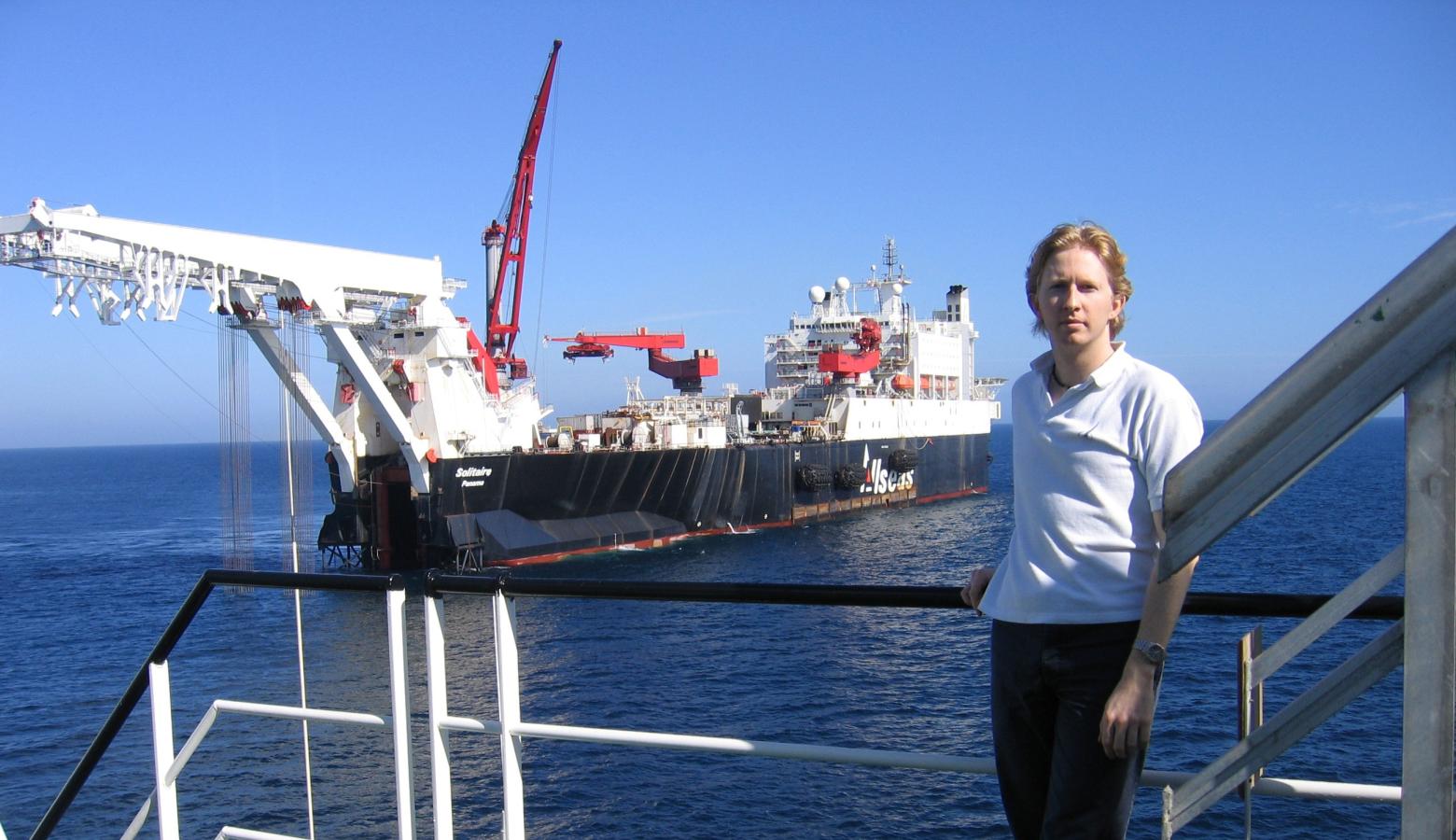 Caspar stands confidently on a railing next to a ship, taking in the surrounding maritime scenery.